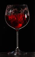 Shiny glass of red wine with splash, at black background