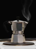 Close-up of the shiny, metallic coffee pot with steam, at black background