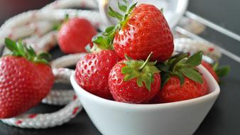 Close-up of the beautiful, shiny, red strawberries with green leaves, white bowl and rope