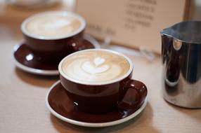Cups of coffee, with the beautiful drawings near the shiny pitcher