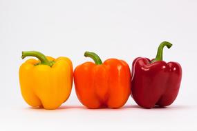 Beautiful and colorful, shiny paprika peppers with green twigs, on the white surface