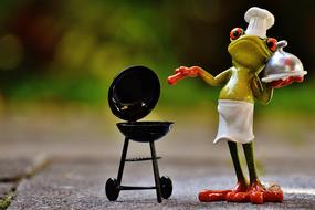 Colorful, shiny figure of the frog cook in hat, near the grill