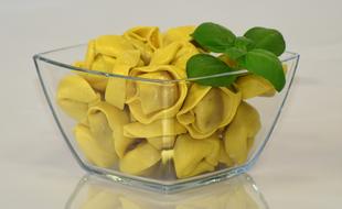 Beautiful, yellow tortellini pasta with green leaves, in the glass bowl, with reflection