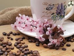 Close-up of the beautiful still life with the colorful, patterned cup on the saucer with colorful flowers, near the coffee beans