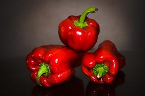 three bright red peppers on a dark background