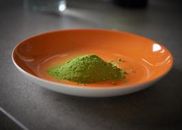 Close-up of the green Moringa Oleifera leaf powder on the shiny, orange plate