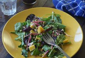 Close-up of the colorful salad with mango, on the yellow plate with fork, on the wooden table