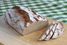 Loaf of the beautiful, brown bread, on the wooden board, on the green and white checkered cloth