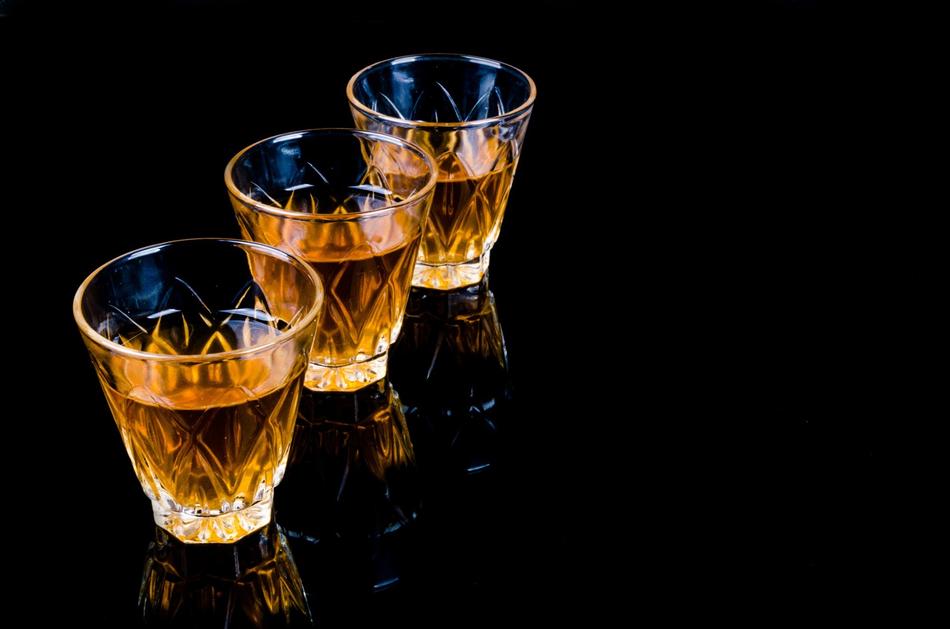 three glasses with alcohol on a black table