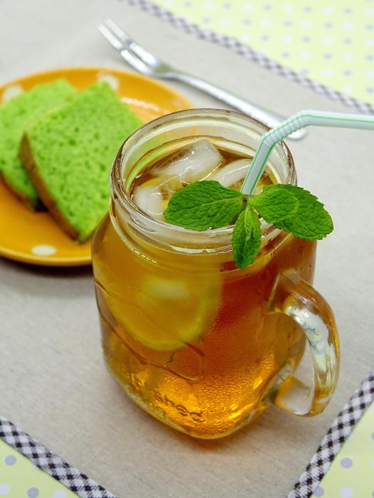 Beautiful and colorful ice lemon tea with fruits and straw, near the dessert on the plate