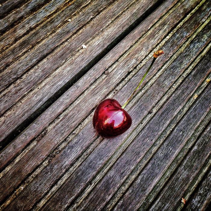 Close-up of the beautiful, shiny, red cherry, on the wooden surface, in light