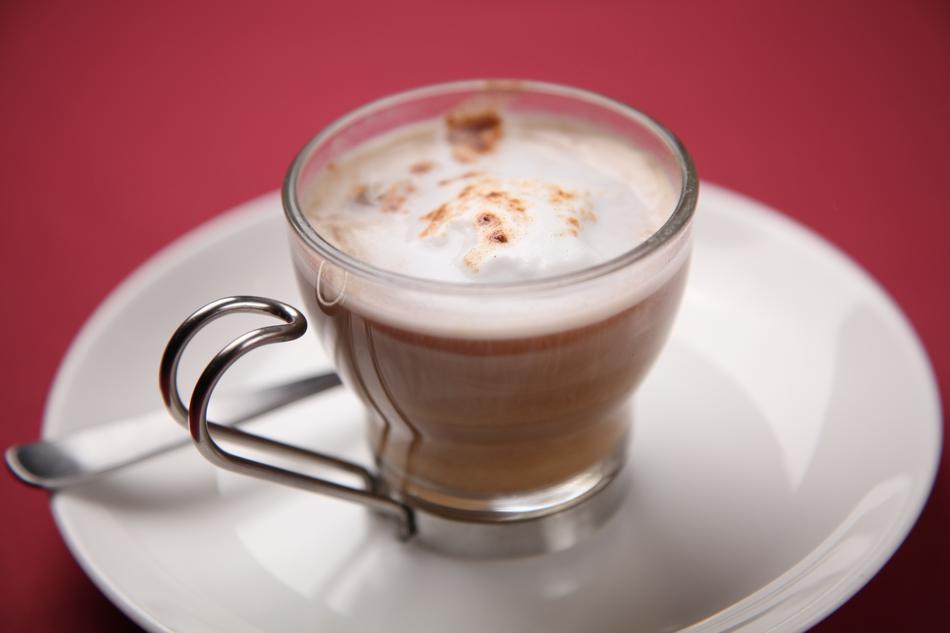 Shiny glass of cappuccino, on the white saucer with spoon, on the red surface
