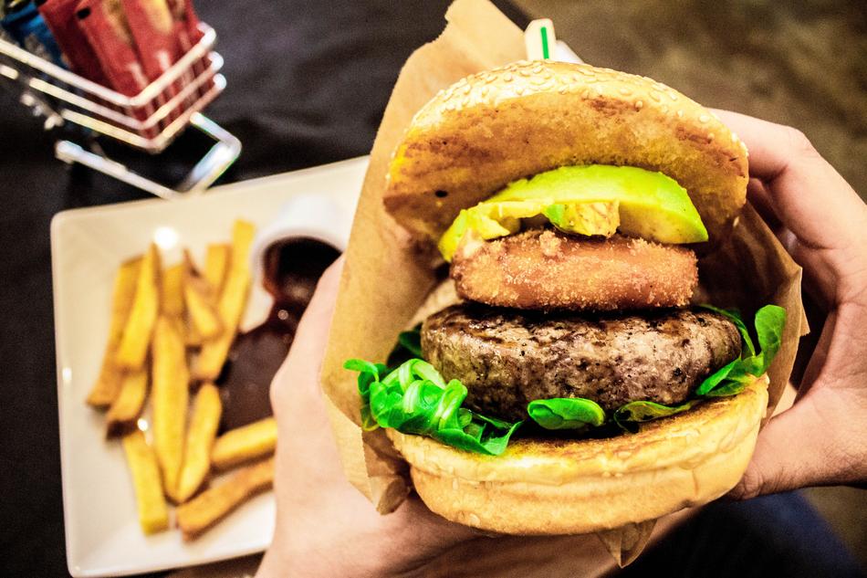 beautiful and colorful burger with vegetables, in the hands, above the plate with fried potatoes