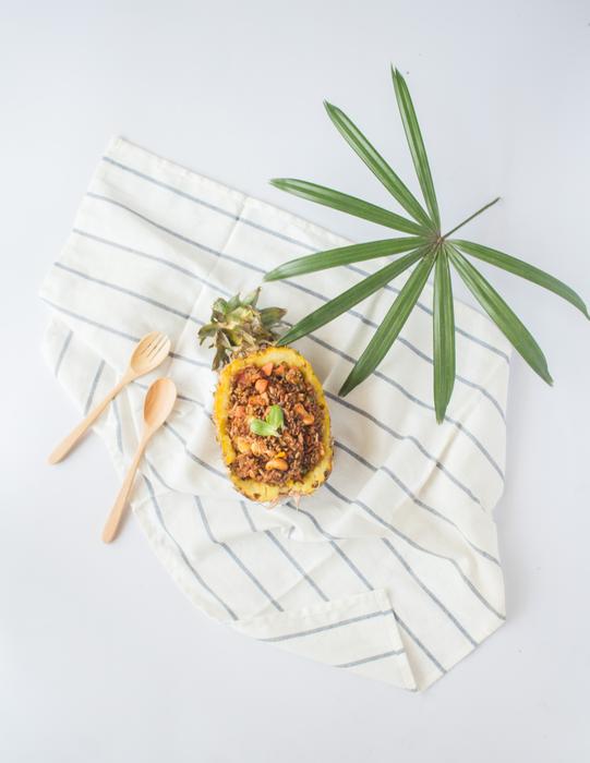 Beautiful and colorful food with pineapple, near the green leaves and wooden spoons on the cloth with stripes