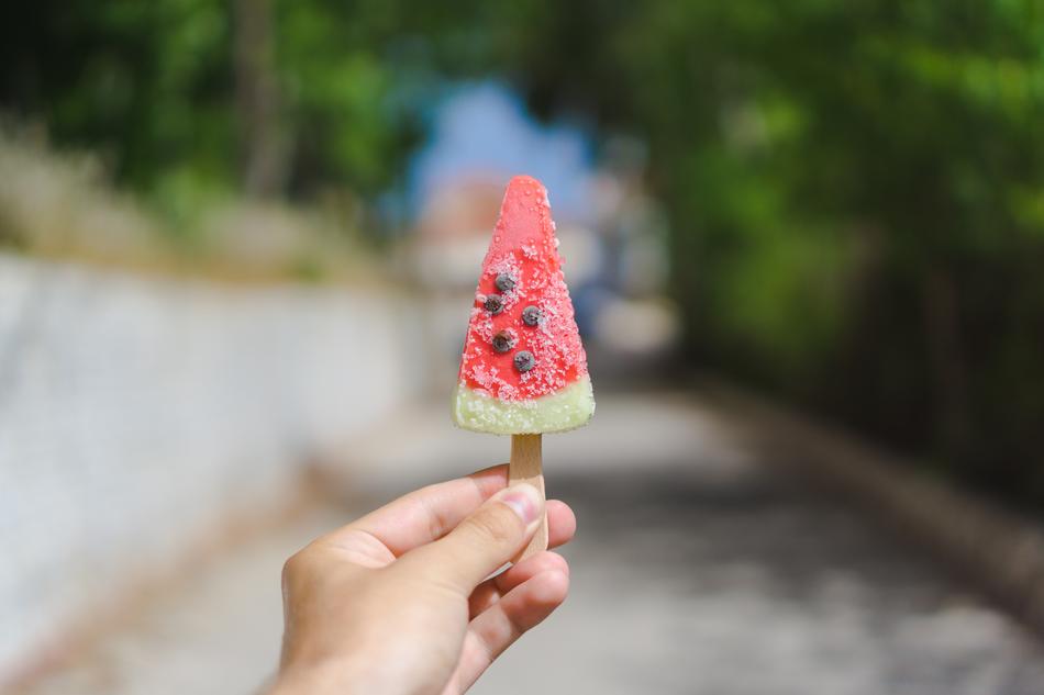 frozen piece of watermelon on stick in child’s hand, blur background