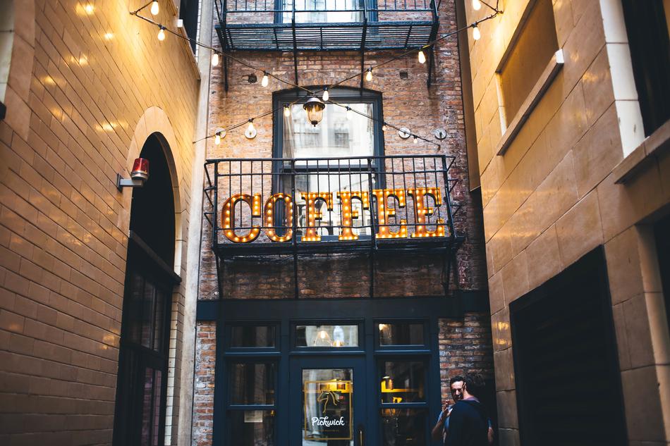 People near the building with windows, lights and 'COFFEE' sign