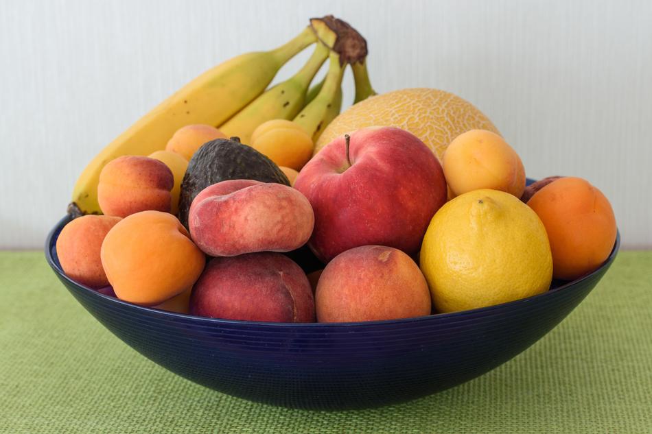 Dark bowl of the colorful and beautiful fruits, on the green surface