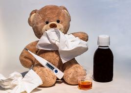 teddy bear with a thermometer and a scarf and medicine on the table