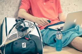 young boy sits with laptop at wall near bag with sports equipment