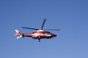 Red and white Helicopter in flight at blue sky background