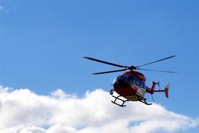 Flying, shiny helicopter, at blue sky with white clouds on background