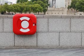 Red and white aid buoy, in the container, on the wall, near the water, green trees and buildings