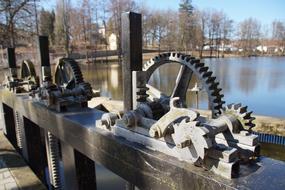 Close-up of the floodgate with gears and beautiful shore with the trees