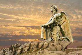 Beautiful statue of the angle, among the rocks, at colorful sunset with clouds