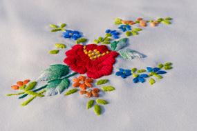 Colorful and beautiful embroidery with the flowers, on the stems, with the leaves, on the white fabric