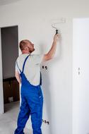 male Painter works with roller at wall indoor