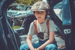 a boy sitting near an old car