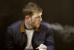 young caucasian man with tattoo on neck smoking