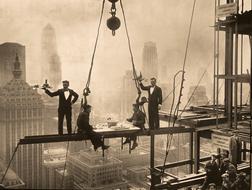 waiters beside of two men dining on metal beam on skyscraper under construction by American photographer Charles C. Ebbets