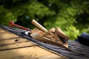 Close-up of the tools and belt on the black roof of the wooden house, near the green plants