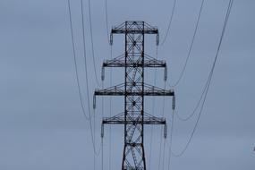 View of the electricity pylon at gray, cloudy sky background