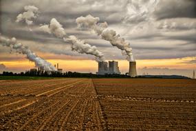 smoking Power Plant behind plowed field at sunset