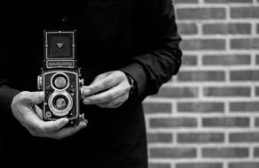 Black and white photo with the close-up of the beautiful, vintage Rolleicord camera in the hands of the photographers, near the brick wall