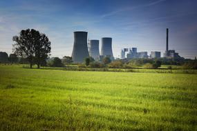 Nuclear plant, behind the colorful and beautiful field, with the plants, under the blue sky with clouds