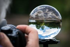 Photographer with the camera, taking a photo of the beautiful, shiny glass ball, with the landscape with the green trees