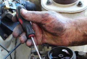 dirty Hand of Mechanic with tool at Carburetor