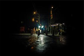 workers in helmets stand at a lamppost on a night street