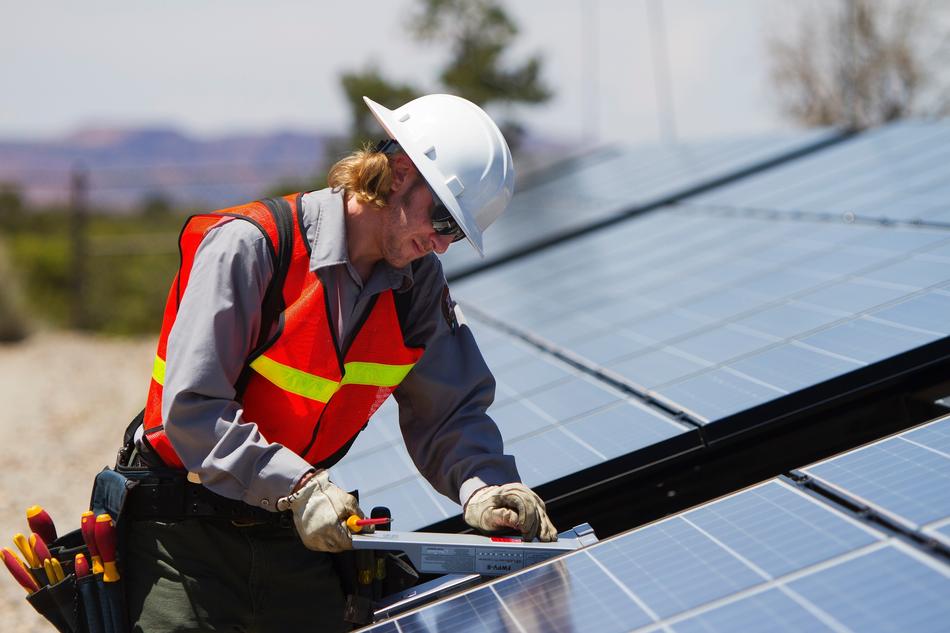 Man worker, in the uniform and white helmet, near the solar panels, on the landscape
