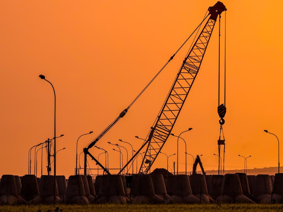 construction crane and street lights at construction site against orange sky background