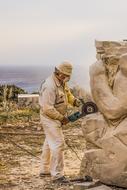Artist Man Sculptor with circular saw works at sculpture in park, cyprus, ayia napa