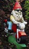 Colorful garden dwarf on the motorcycle among the plants