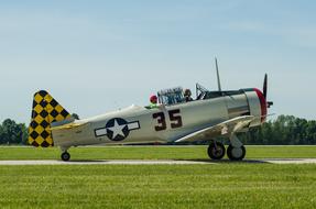 People in the colorful Warbird airplane, on the green field, near the green trees