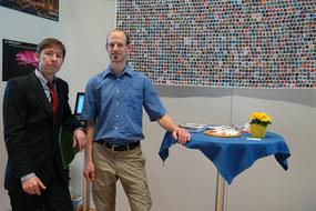 Men, standing near the Trade fair stand, together