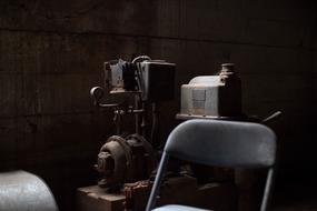 Old chair, near the rusty machine, in light, among the darkness