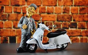 Figure of a man with white Vespa motor scooter near the brick wall