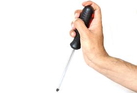 Holding metal screwdriver with black and red handle, in hand, at white background